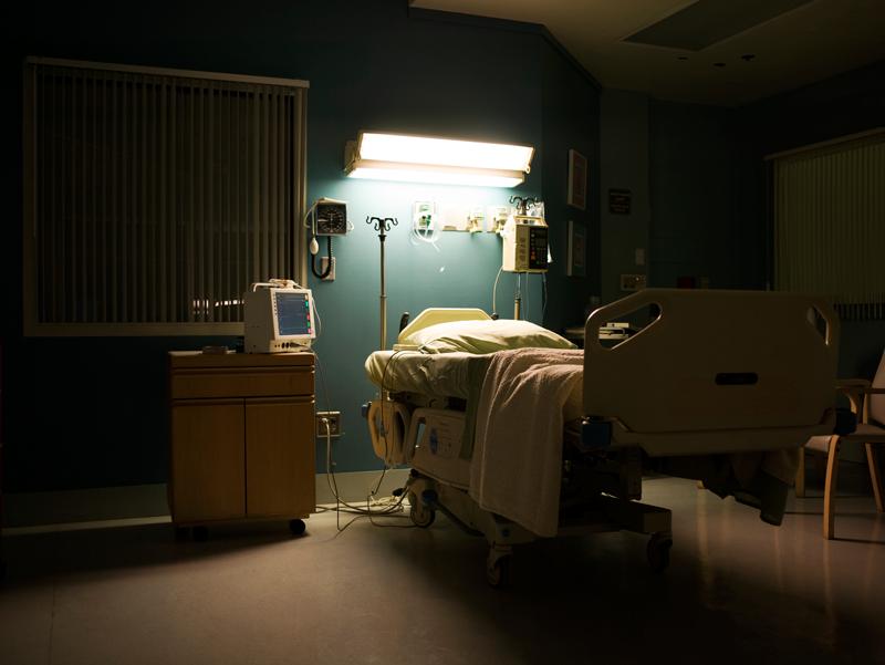 Darkened hospital room with light on over bed